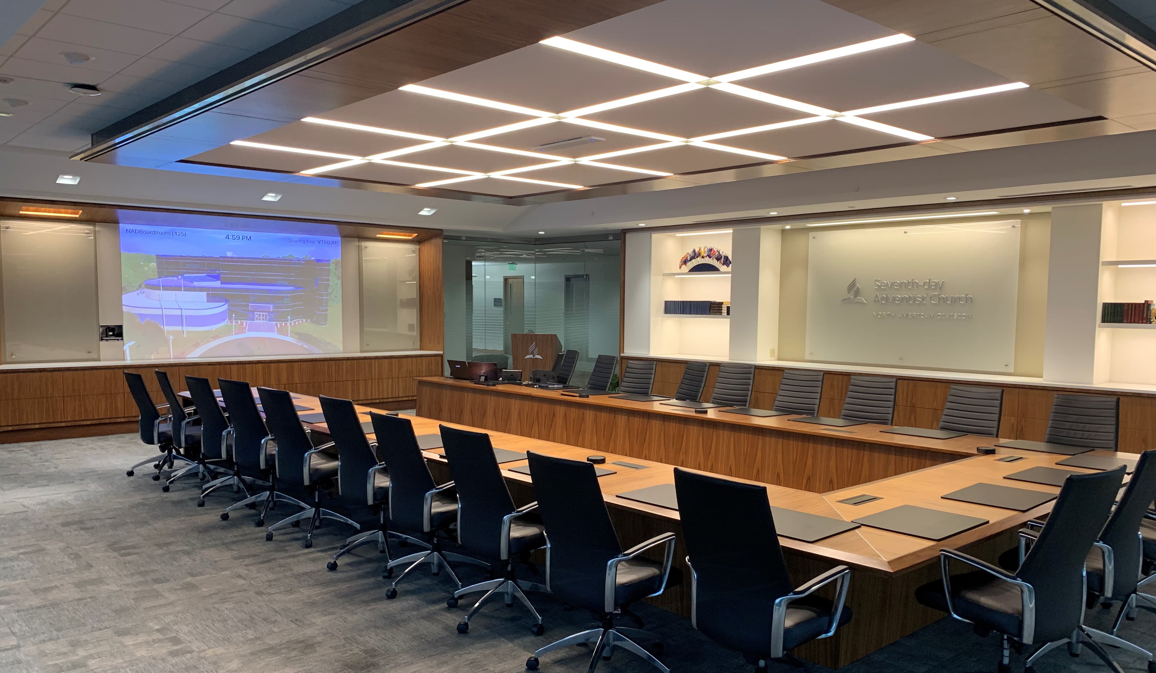 Executive boardroom with long wooden conference table, integrated ceiling lighting, and a wall-mounted projection screen