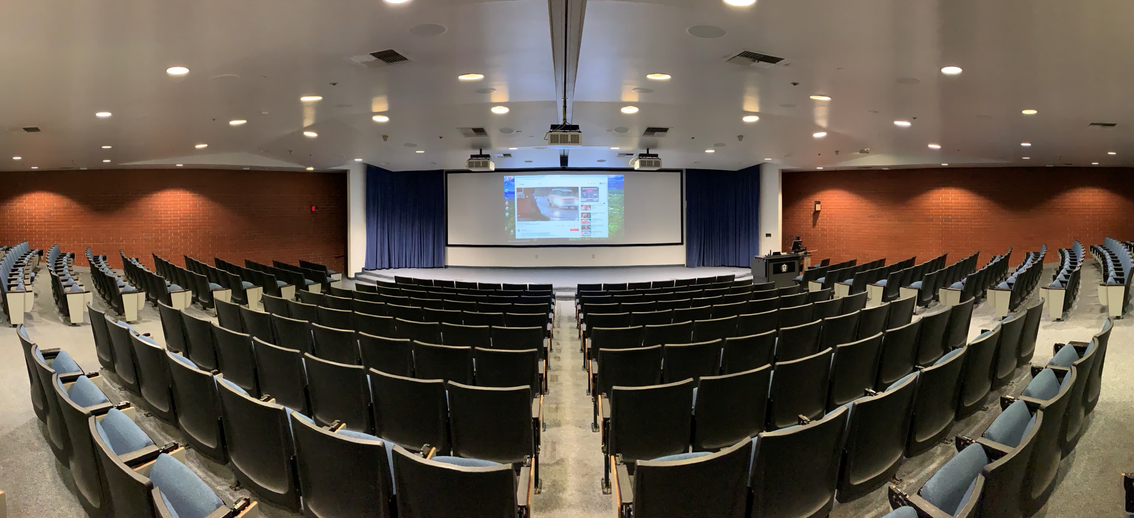Panoramic view of a university lecture hall with rows of seating and a center-projection screen