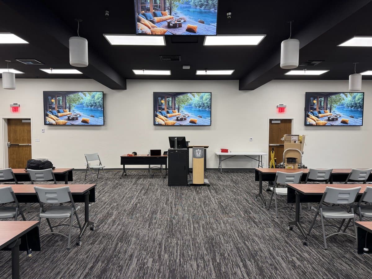 Training room with triple ceiling-mounted displays, podium, and classroom seating